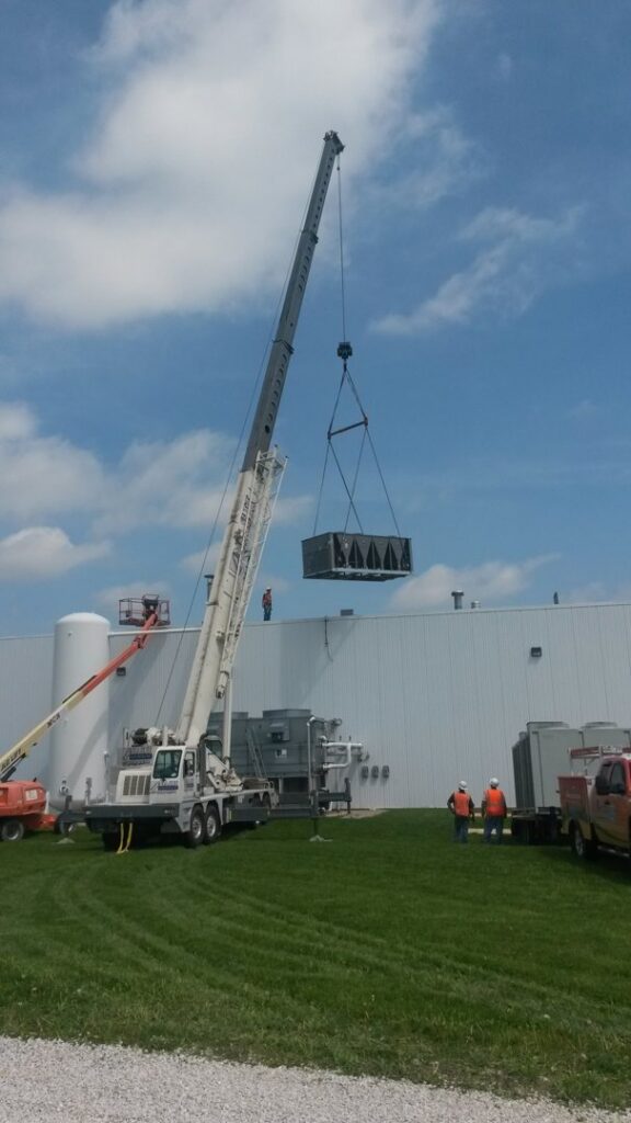 A crane lifting a large commercial HVAC unit onto a building roof by Michael Savage-Lanz Heating & Cooling in Champaign, IL