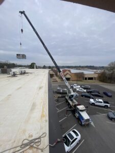 A large commercial HVAC unit being lifted by a crane onto a building rooftop by Comfort Engineering Co Inc in Tupelo, MS