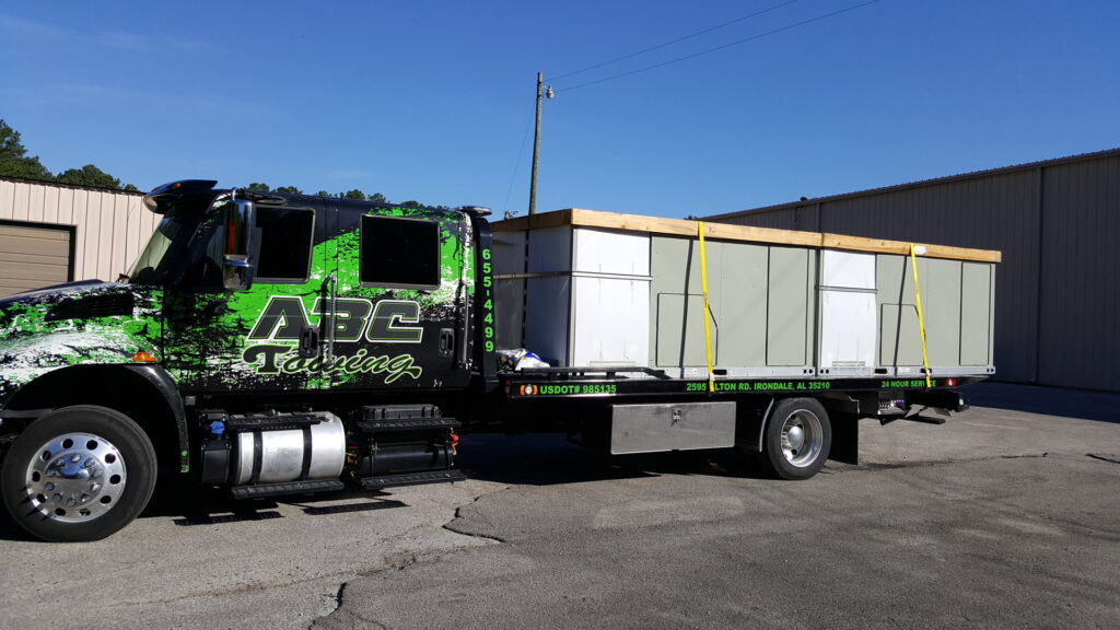 A tow truck transports a large commercial HVAC unit for Perry Tillman TM Air Engineers in Birmingham, AL.
