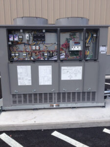 A commercial HVAC unit with its electrical panels open, showing wiring and components, serviced by ACI Northwest Heating, Cooling & Electrical in Dalton Gardens, ID.