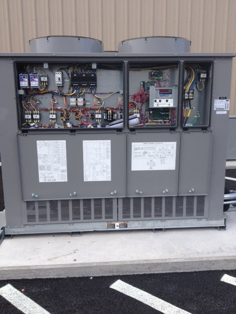 A commercial HVAC unit with its electrical panels open, showing wiring and components, serviced by ACI Northwest Heating, Cooling & Electrical in Dalton Gardens, ID.