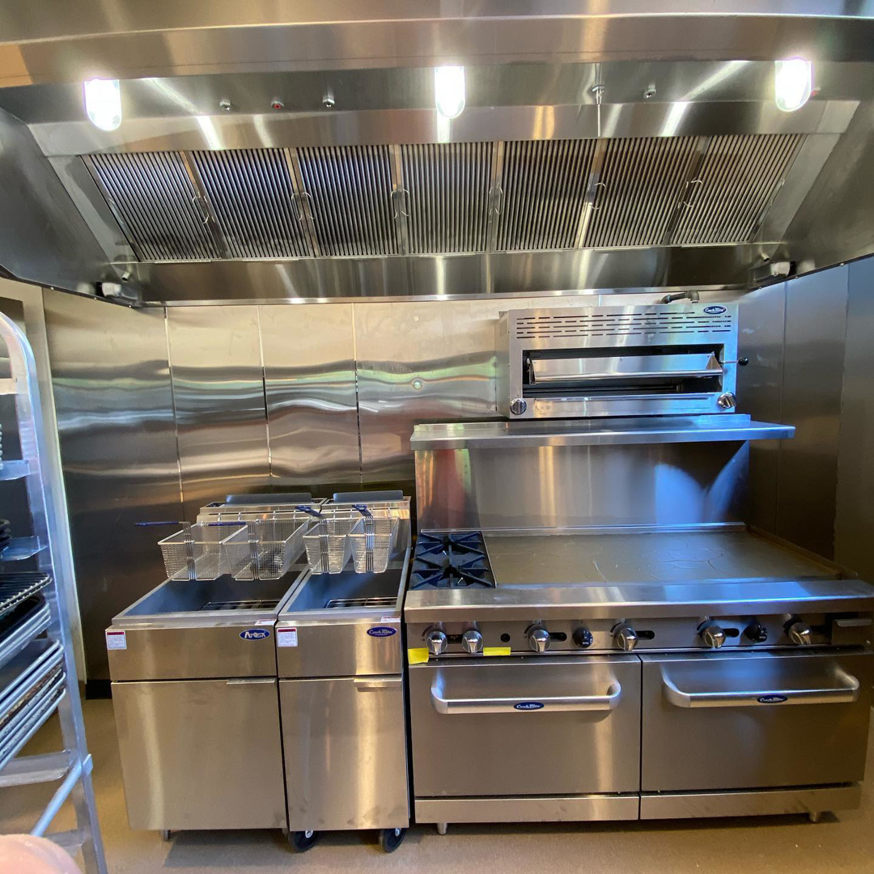 A commercial kitchen featuring a large stainless steel exhaust hood system installed by Mech-Masters, Inc. in Nampa, ID.