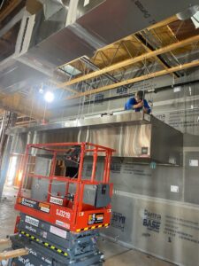 A technician installing a large commercial kitchen hood and exhaust system by Dowd Heat & Air in Tulsa, OK.