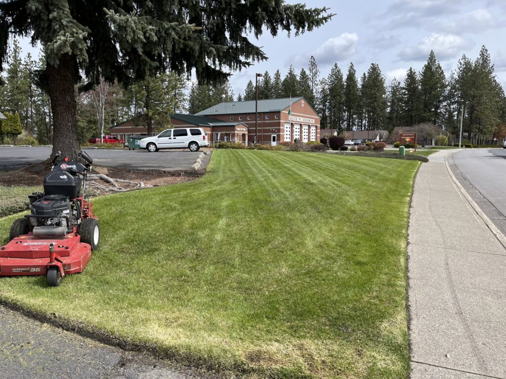 A commercial walk-behind lawn mower parked on a freshly mowed lawn with distinct stripes at a business property by McLain Lawn & Landscape in Spokane, WA.