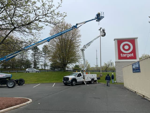 A commercial lighting installation site with multiple boom lifts and service trucks from Lighting Services, Inc. in Waterbury, CT.