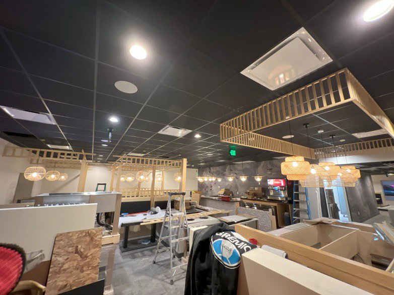 Commercial interior under construction with exposed ceiling grid and various light fixtures being installed by Homestead Electric in Orem, UT.