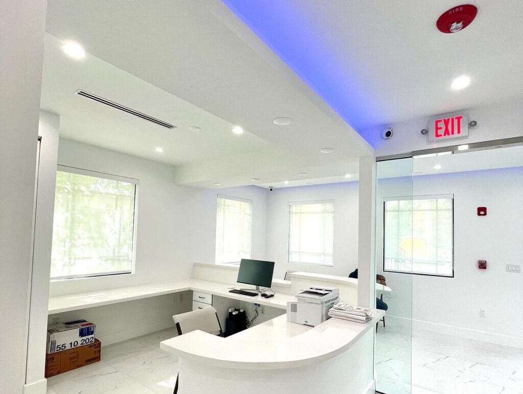 A modern commercial office reception area with new recessed lighting, blue LED strip lights, and an exit sign installed by CityWide Electrical Service LLC in Hialeah, FL.