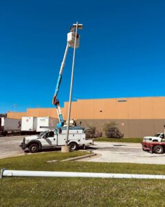 An electrician in a bucket truck repairing a commercial parking lot light pole for Pure Light Electric in Kansas City, MO.