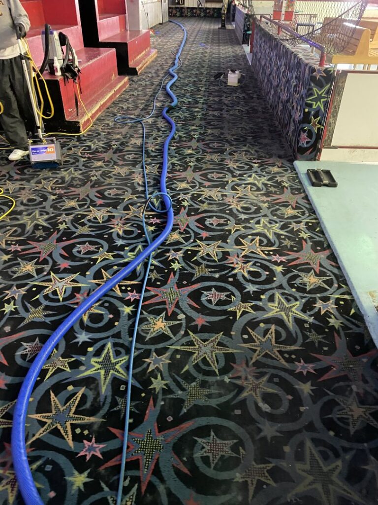 A vibrant, patterned commercial carpet being cleaned with professional equipment and hoses by B of C Carpet Cleaning LLC in Idaho Falls, ID.