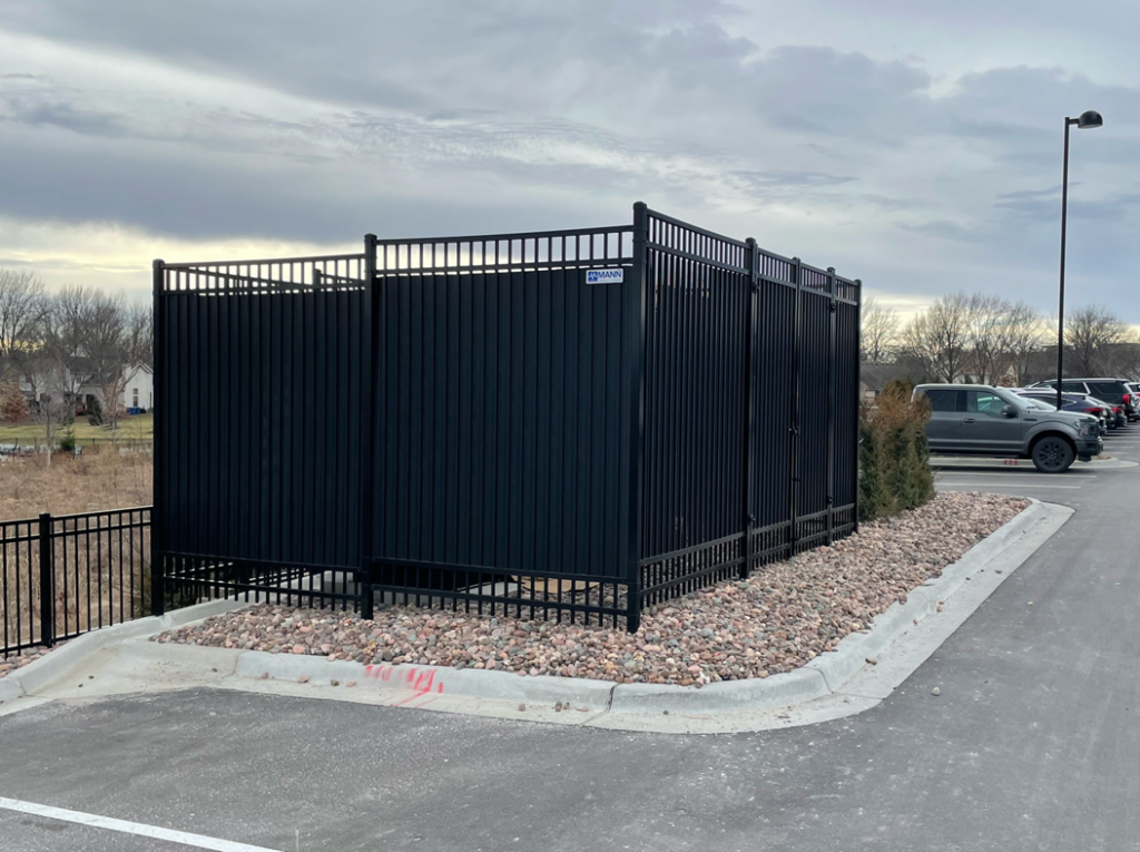 Side view of a black commercial privacy fence enclosure installed by Mann Fence Co., Inc. in Olathe, KS.