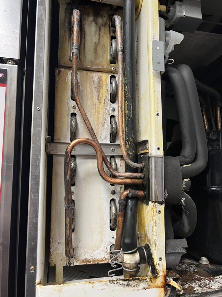Internal view of dirty copper refrigeration coils and lines in a commercial unit, indicating service by Commercial Kitchen Services, LLC of Watertown, SD.
