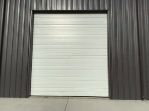 A white commercial roll-up garage door installed on a dark grey corrugated building by Magic City Door Huntsville in Birmingham, AL.