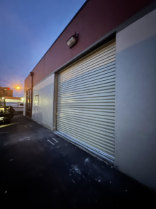A commercial roll-up garage door on a building exterior at dusk, installed by Roll-Rite Garage Doors in Denver, CO.