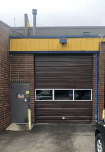A brown commercial roll-up garage door on a brick building, installed by 170 Springs LLC Garage Doors in Aurora, CO
