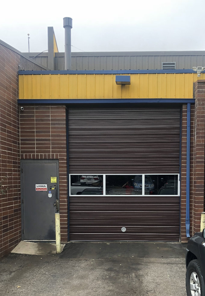 A brown commercial roll-up garage door on a brick building, installed by 170 Springs LLC Garage Doors in Aurora, CO