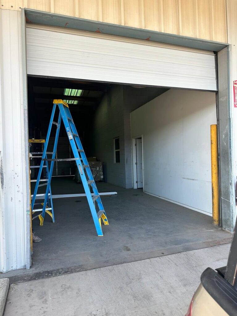 An open commercial roll-up garage door with a ladder inside, indicating service by Central Garage Door Repair LLC in Glendale, AZ.