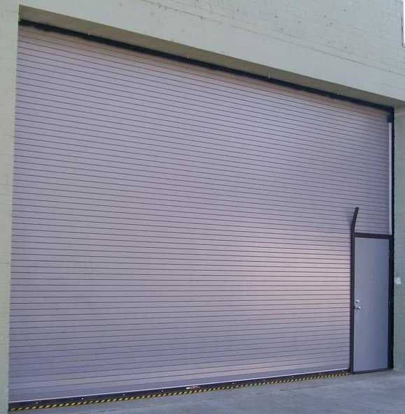 A commercial rolling garage door with an integrated pedestrian door, installed by Overhead Door Company of Maricopa & Pinal County in Mesa, AZ.