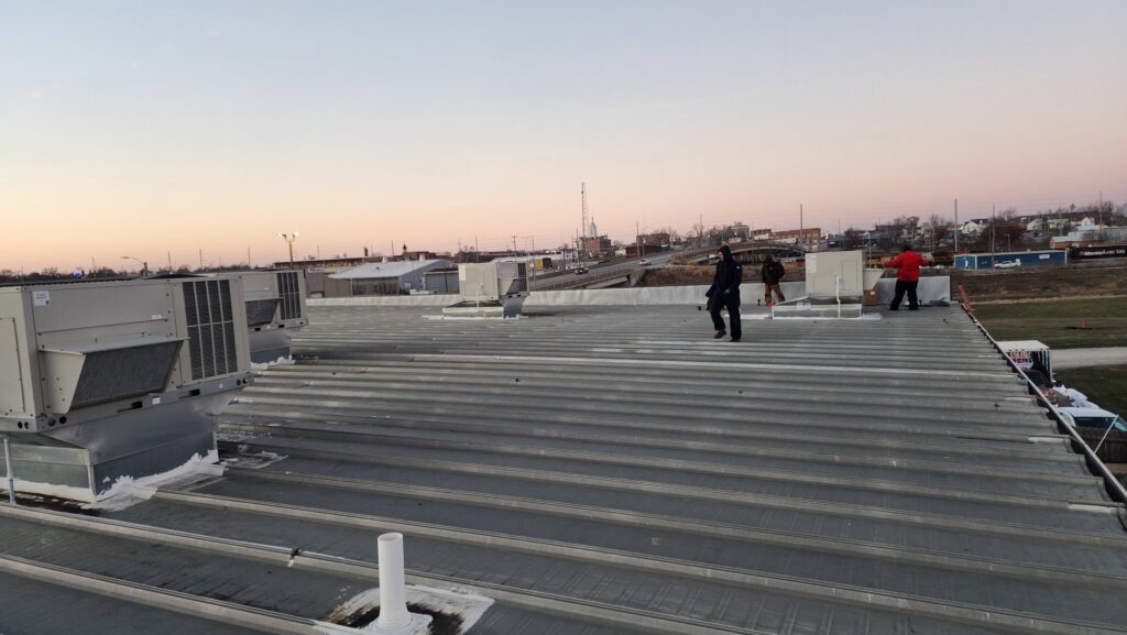 Multiple commercial rooftop HVAC units installed on a large building with technicians on the roof by PNW Spokane Heating and Air in Spokane, WA.