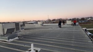 Multiple commercial rooftop HVAC units installed on a large building with technicians on the roof by PNW Spokane Heating and Air in Spokane, WA.