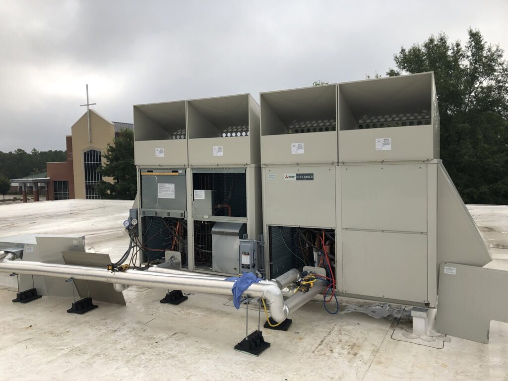 Multiple Mitsubishi commercial HVAC units on a rooftop undergoing service or repair by Deon Arnold Heating & Air Conditioning in Fayetteville, NC
