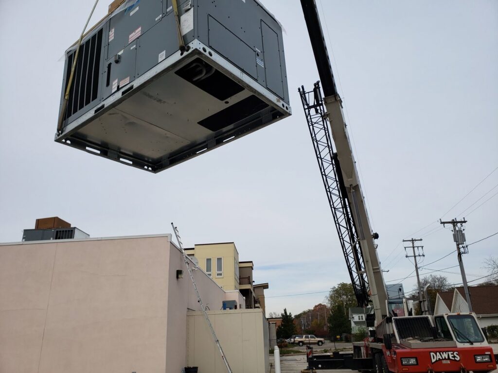 A large commercial rooftop HVAC unit being lifted by a crane during installation by 9-1-1 Heating & Air, LLC in Milwaukee, WI.