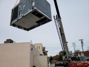 A large commercial rooftop HVAC unit being lifted by a crane during installation by 9-1-1 Heating & Air, LLC in Milwaukee, WI.