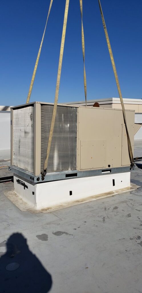 A large commercial rooftop HVAC unit being lifted for installation or removal by DMC Service, Inc. in Olathe, KS.