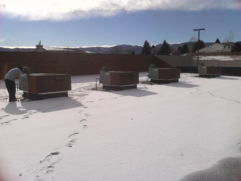 An HVAC technician servicing a commercial rooftop HVAC unit in snowy conditions by Atmosphere Mechanical Heating And Air / Ventilation in Aurora, CO.