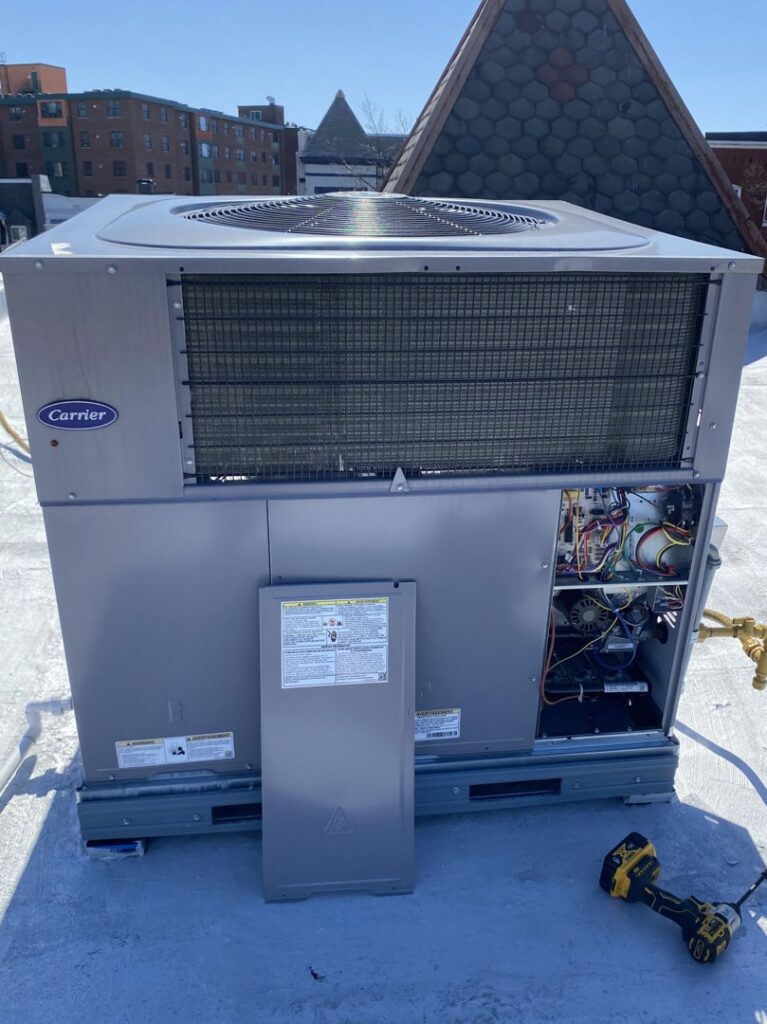 A commercial rooftop HVAC unit (Carrier) with an open access panel undergoing service by Infinite Heating & Air in Newnan, GA.