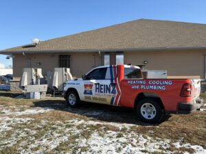 A Heinz HVAC & Plumbing service truck parked near multiple commercial rooftop HVAC units outside a building in Vincennes, IN.