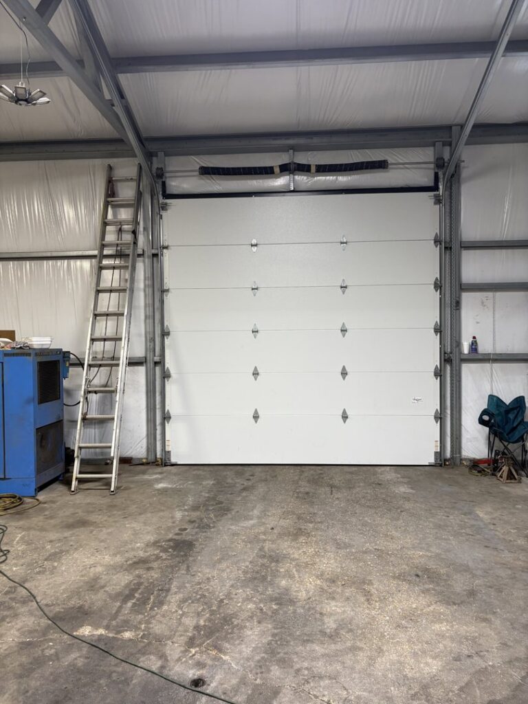 A commercial sectional garage door with a ladder, indicating installation or service by Cajun Doors & More in Lafayette, LA.