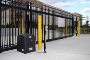 A commercial security gate with yellow bollards and an automatic operator, installed by Overhead Door Company of Maricopa & Pinal County in Mesa, AZ.