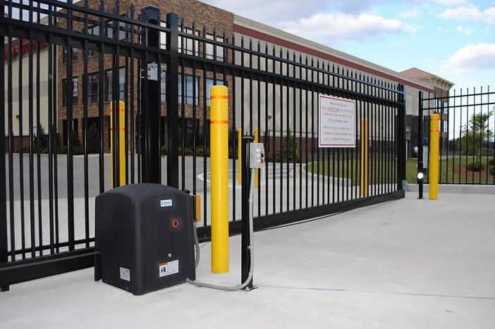 A commercial security gate with yellow bollards and an automatic operator, installed by Overhead Door Company of Maricopa & Pinal County in Mesa, AZ.