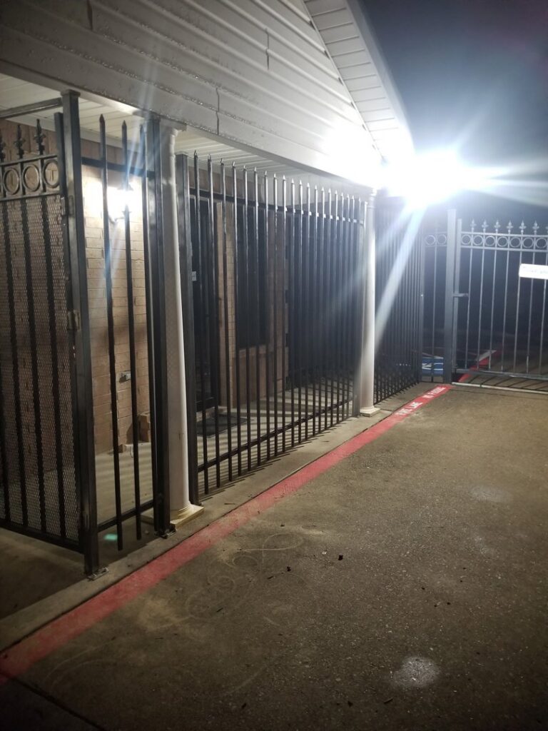 A long commercial security metal fence and gate installed by Dallas Mobile Welder, LLC. at night in Dallas, TX.