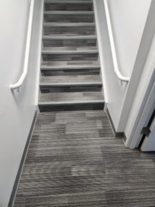A commercial staircase and landing with newly installed striped carpet tiles by Carpet Center in Nashua, NH.
