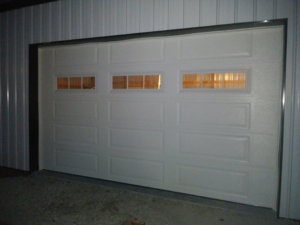A white commercial garage door with three top windows, professionally installed by R&A Overhead Door in Gower, MO.