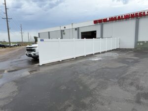 A long white vinyl privacy fence installed next to a commercial building by Bostwick Fencing, LLC in Sioux City, IA.