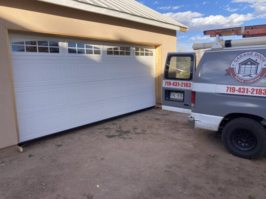 A Garage Door Repair Company, LLC service van parked next to a newly installed white garage door in Pueblo, CO.