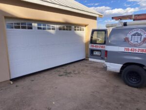 A Garage Door Repair Company, LLC service van parked next to a newly installed white garage door in Pueblo, CO.