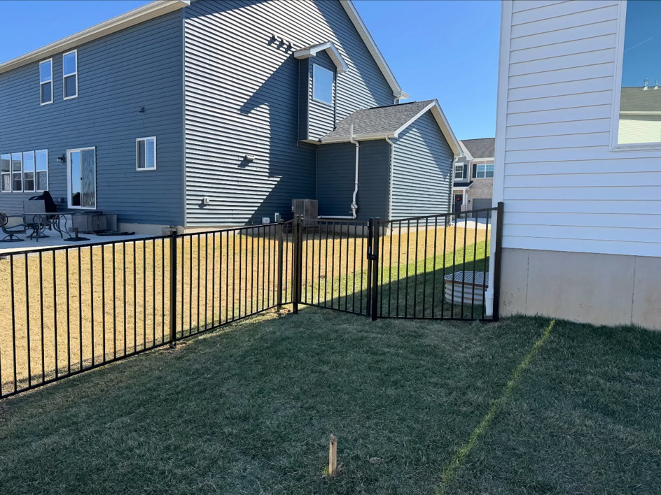 A completed black aluminum fence with a gate installed between two homes by BK FenceWorks in Wentzville, MO.