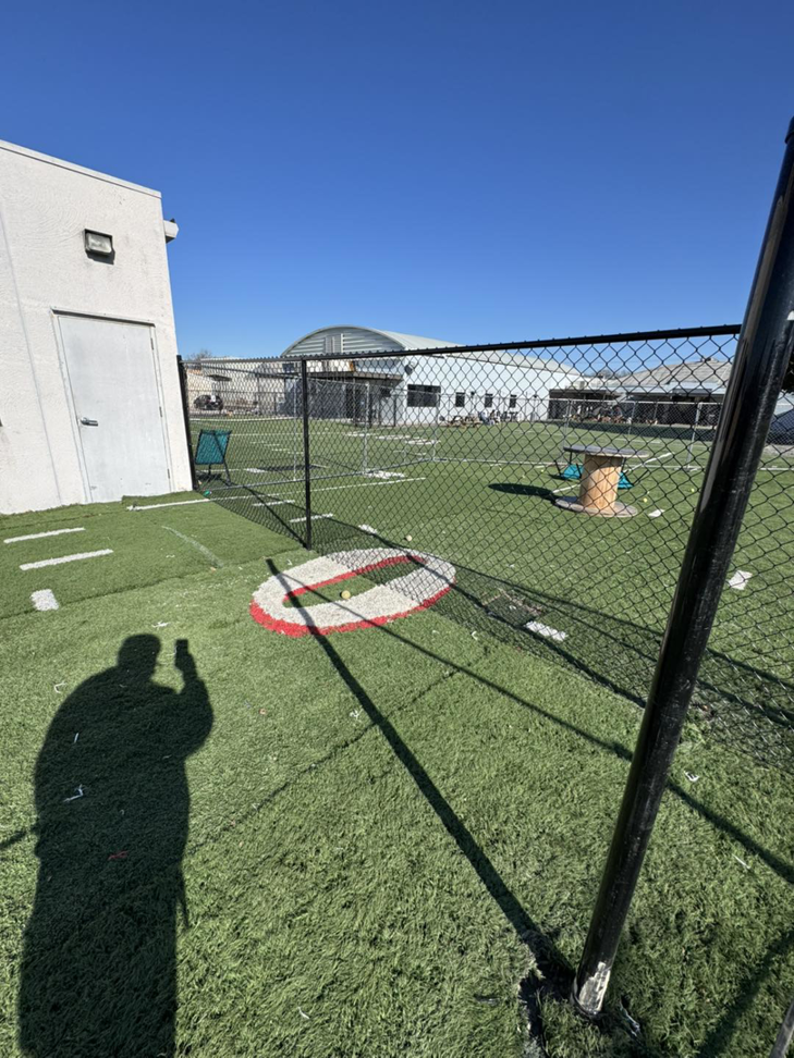 A completed section of black chain-link fence next to a building and artificial turf by Just Handy Fence and Stain LLC in Tulsa, OK.