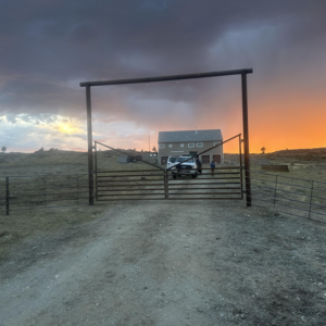 A newly installed metal entrance gate and archway at sunset, completed by Cool Hand Fencing and Wyo War Wagons in Laramie, WY.