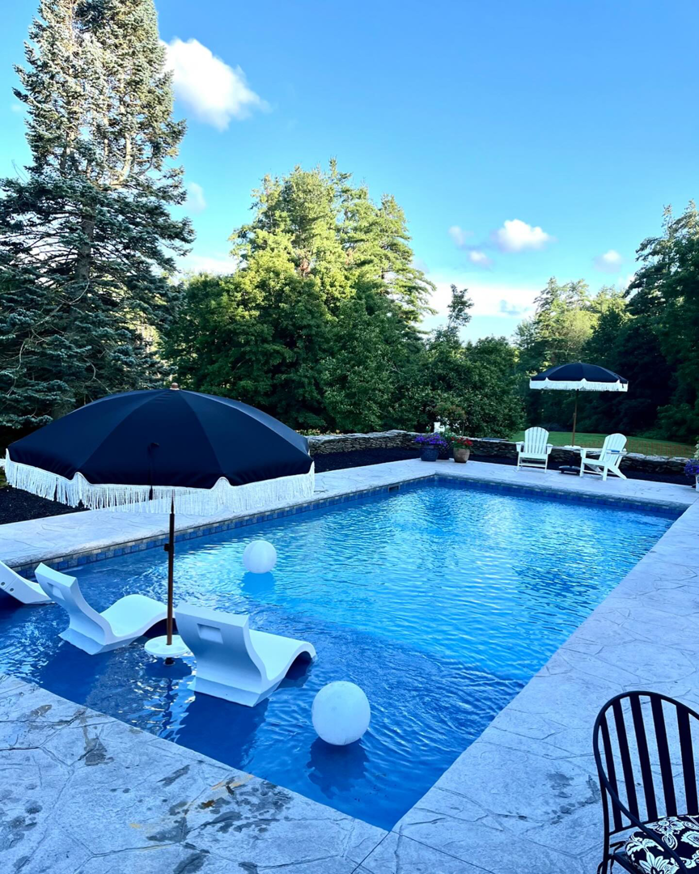 A beautifully completed swimming pool with a stone patio and lounge chairs by MountainScapes in Nashua, NH.