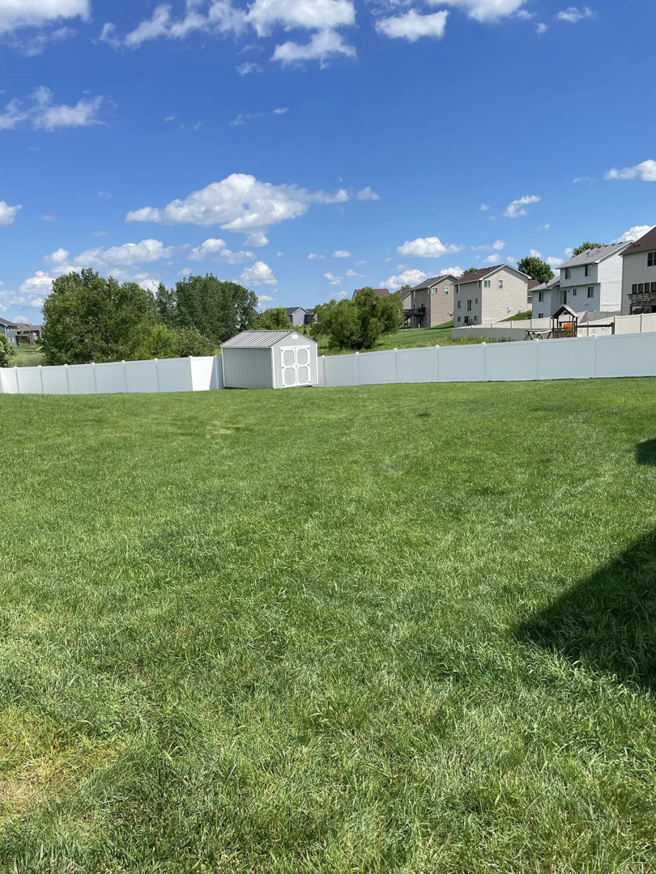A wide view of a completed white vinyl fence enclosing a large backyard with a shed by Flash Fence in Phenix City, AL.