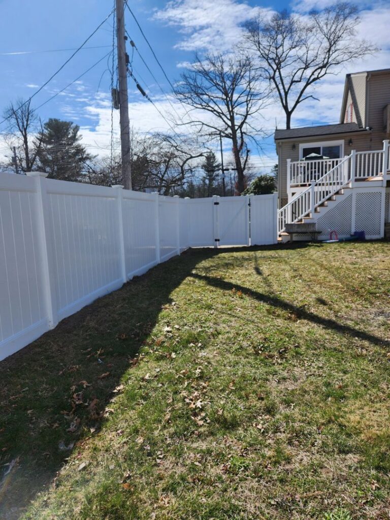 A completed white vinyl privacy fence with a gate installed in a backyard by Matul Fence Inc in Lynn, MA