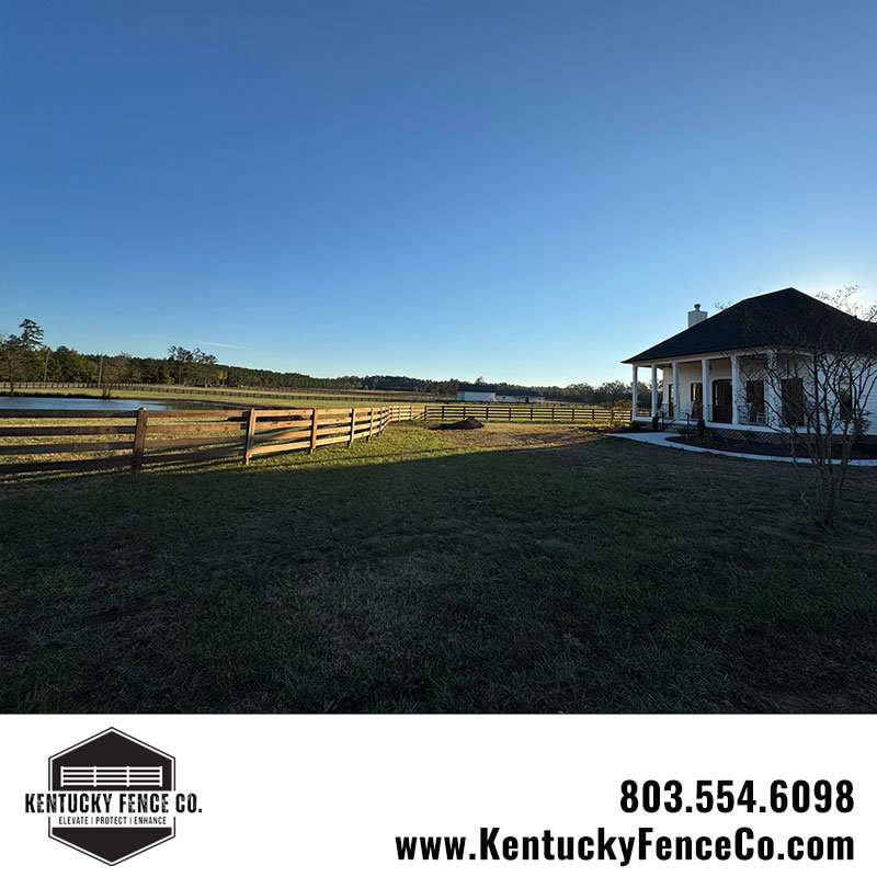 A long view of a completed wooden fence surrounding a property with a house and pond by Kentucky Fence Co in McConnells, SC.