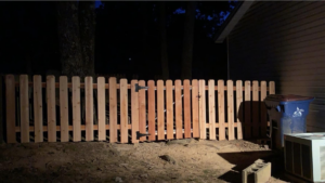 A completed wooden picket fence with a gate, installed by Fianna Fencing Company in Fort Smith, AR, illuminated at night.
