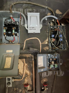 A complex electrical system with open fuse boxes and wiring, including a water heater connection, by CJ Lighting Solution LLC in Greensboro, NC.