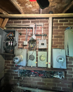 A complex older electrical system with multiple meters, conduits, and an open fuse box, maintained by Sapphire Electric LLC in Jonesboro, GA.