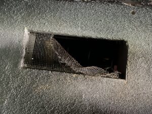 A compromised wall vent with damaged wire mesh, a potential pest entry point, identified by Ark Pest Management in Anaheim, CA.